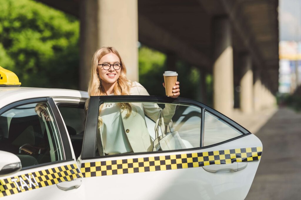 uśmiechnięta blondynka w okularach otwierająca drzwi taksówki